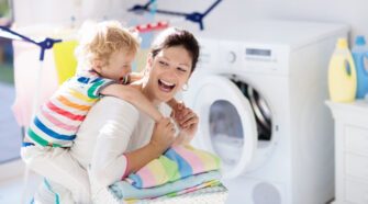 Mother and kids in laundry room with washing machine or tumble dryer. Family chores. Modern household devices and washing detergent in white sunny home. Clean washed clothes on drying rack.