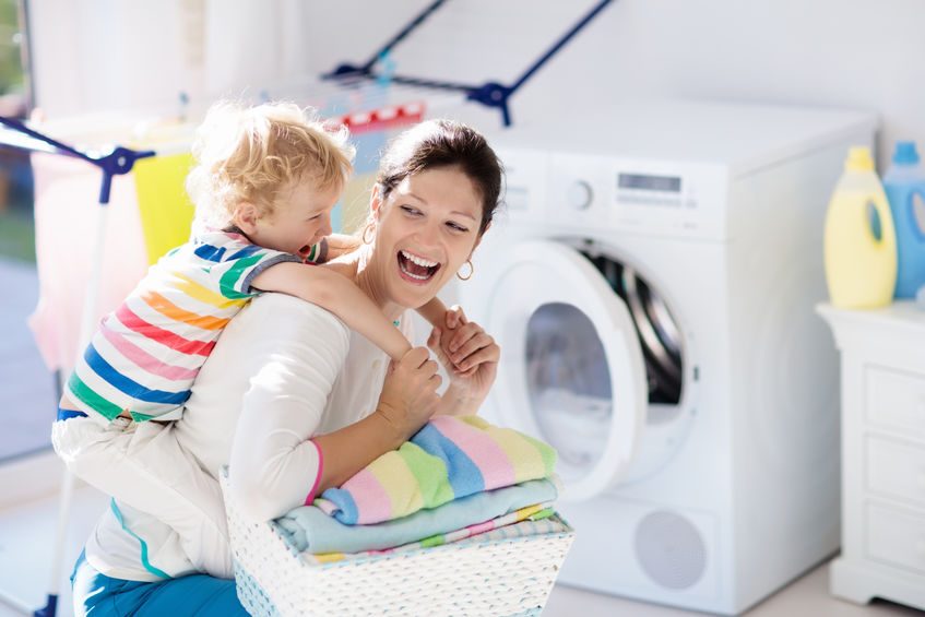 Mother and kids in laundry room with washing machine or tumble dryer. Family chores. Modern household devices and washing detergent in white sunny home. Clean washed clothes on drying rack.