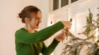 Woman in Green Sweater Hanging A Decor On The Christmas Tree